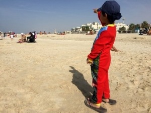 boy from behind pointing at high rises at Jumeira Beach, traveling with kids